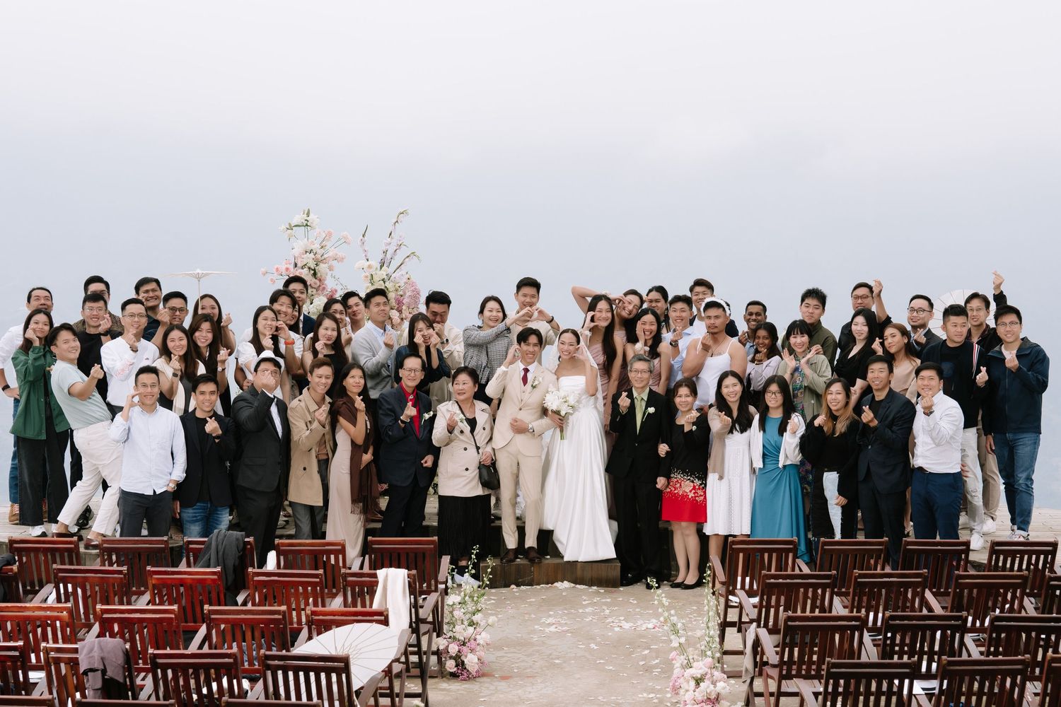 Large wedding group photo with bride and groom surrounded by guests at outdoor mountain ceremony venue.