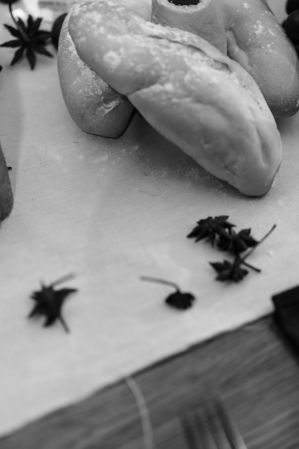 Black and white photo of fresh bread loaves dusted with flour alongside star anise spices on parchment paper.
