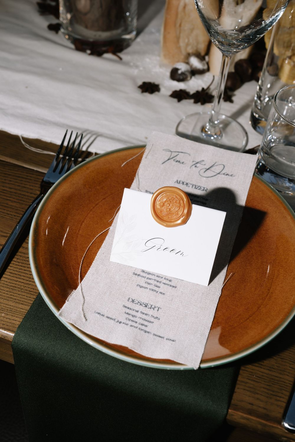 Elegant wedding place setting with terracotta plate, green napkin, and menu card sealed with gold wax stamp.