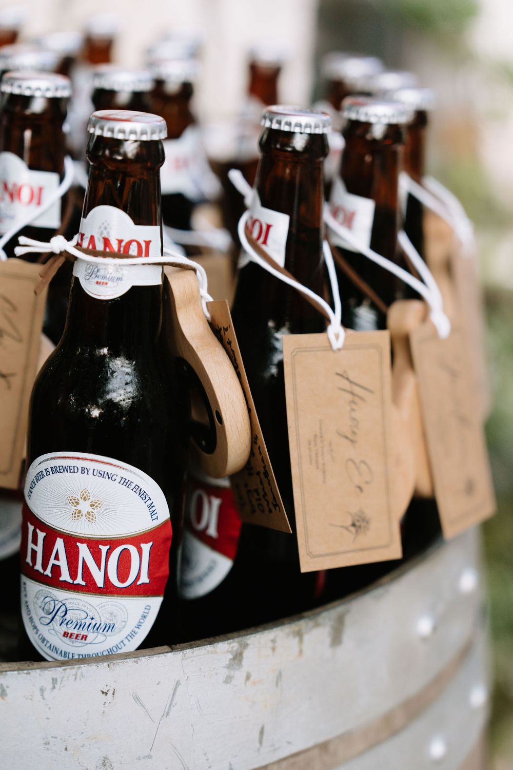 Hanoi Premium Beer bottles with kraft paper gift tags displayed in a rustic wooden barrel at an event.