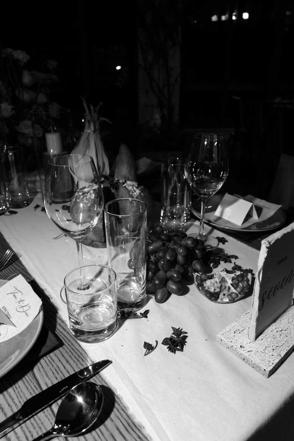 Black and white photo of formal dinner table with wine glasses, grapes, candles, and elegant place settings.