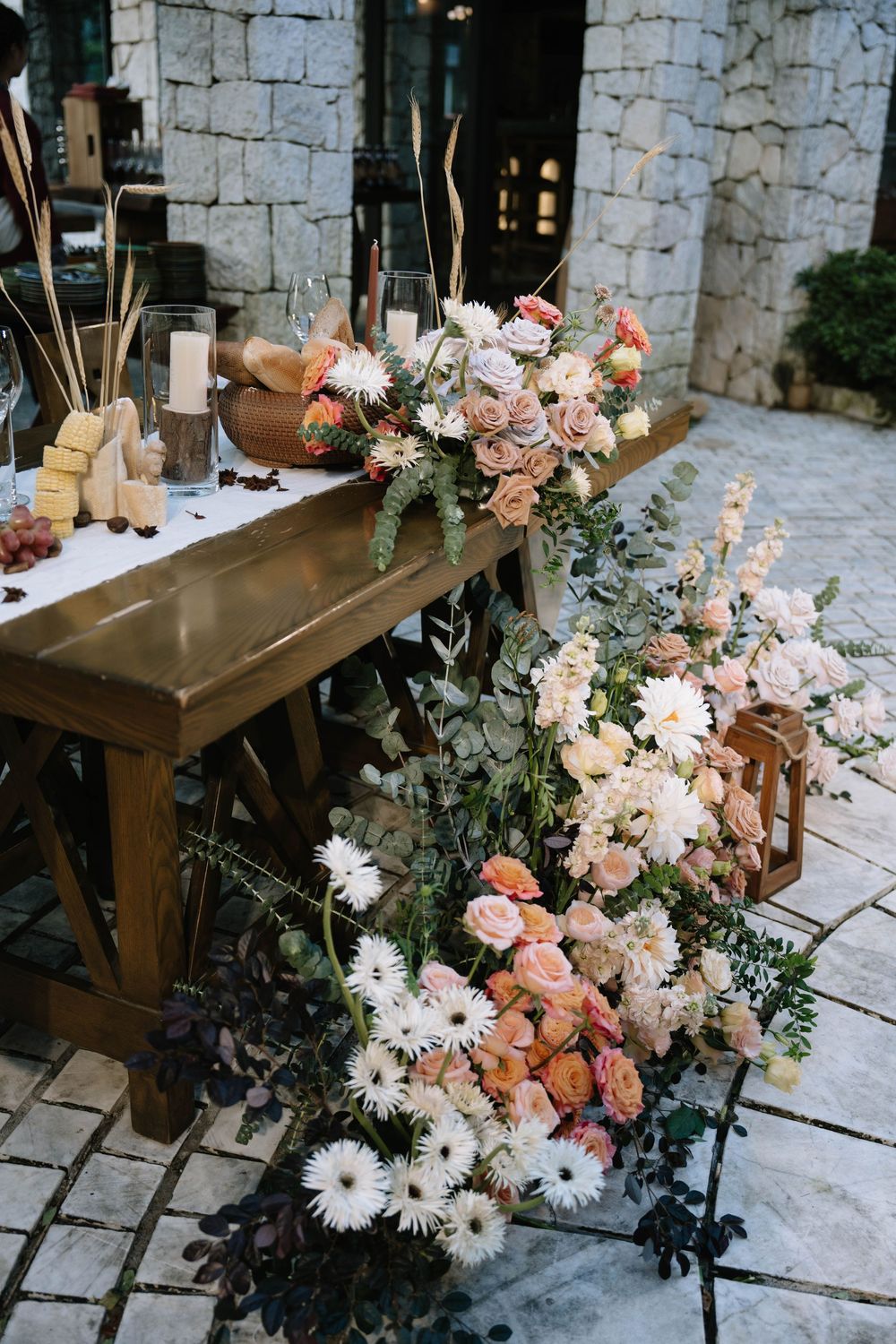 Lush floral arrangement of peach roses, white gerberas, and greenery cascading along a rustic wooden wedding table.