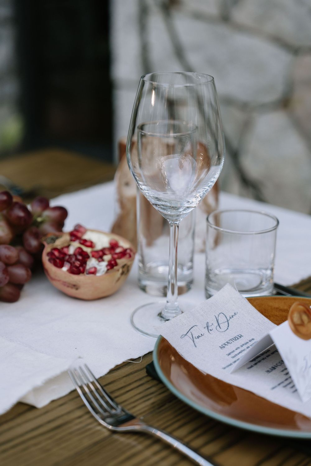 Elegant wedding table setting with wine glass, pomegranate, grapes, amber plate, fork, and menu card.