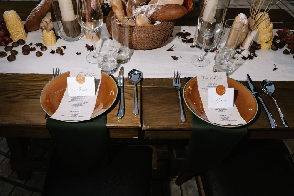 Overhead view of autumn wedding table with amber plates, menu cards, candles, corn, and bread basket.