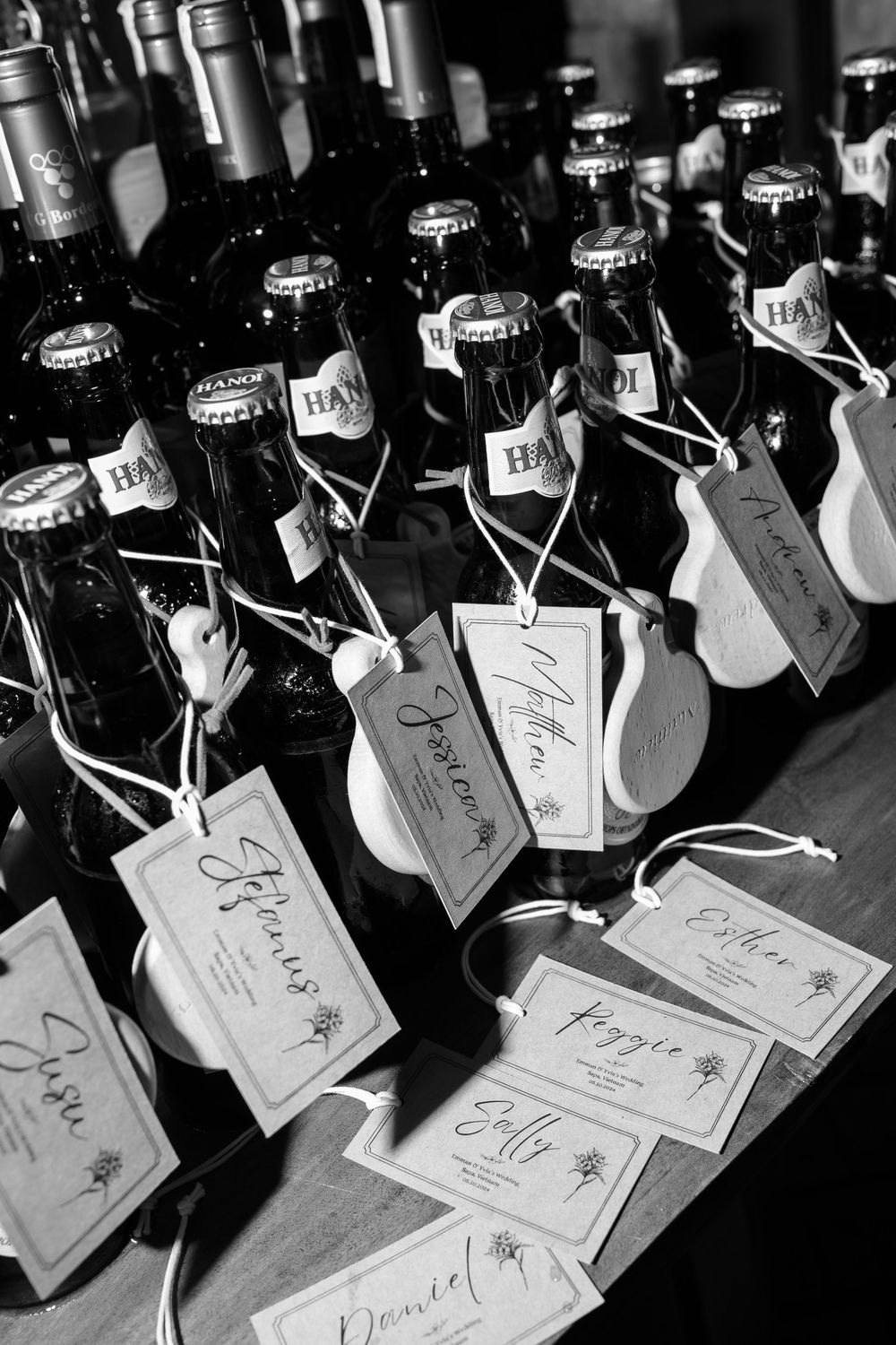 Black and white photo of labeled wine bottle wedding favors with calligraphy name tags on display.