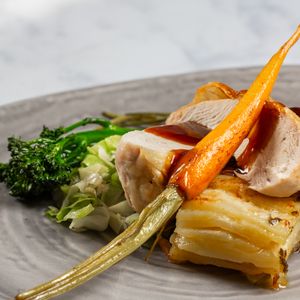 Elegant plated dish showing progression of assembling cooked fish with roasted vegetables on grey plates.