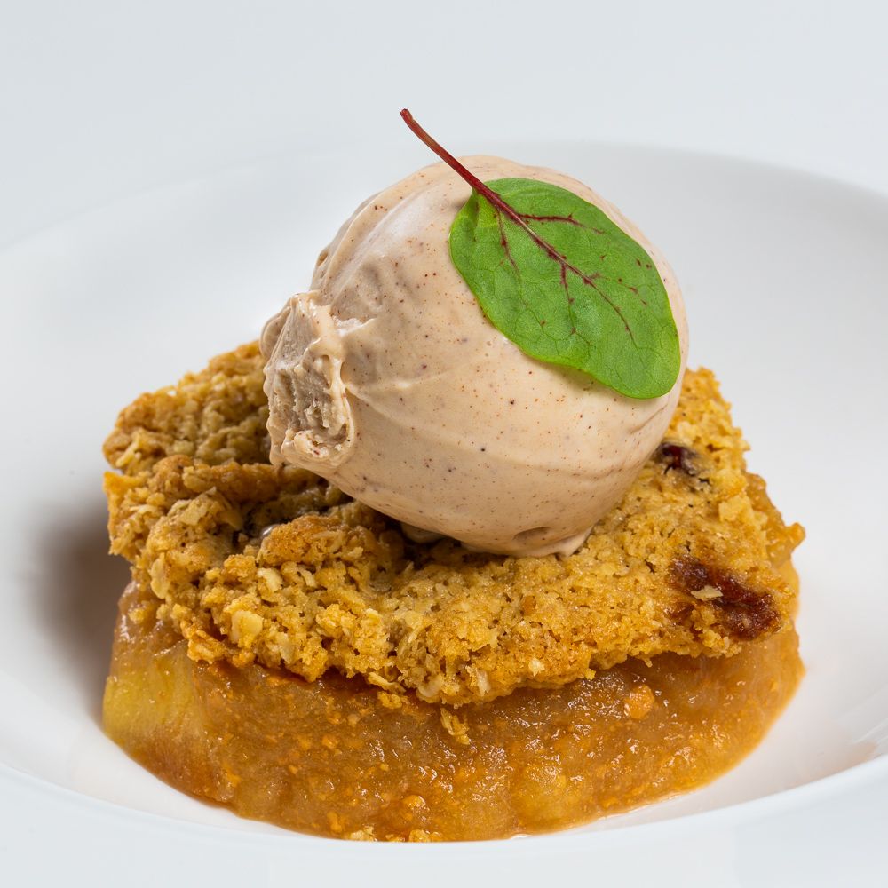 A crispy breaded cutlet topped with chocolate ice cream and fresh basil leaf in a caramel sauce on white plate.