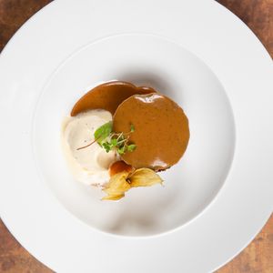 Three white plates with creamy soup and brown sauce garnished with microgreens on a rustic brown surface.
