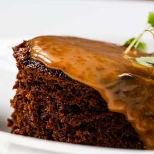 A slice of moist chocolate cake topped with glossy caramel sauce dripping down the sides on a white plate.