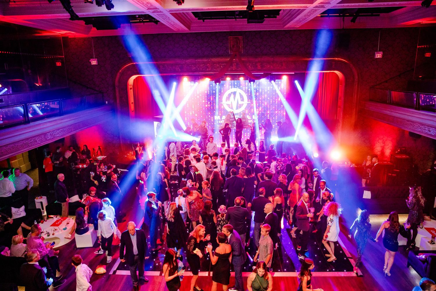 Club dance floor filled with people dancing under vibrant purple lighting at a nighttime party event.