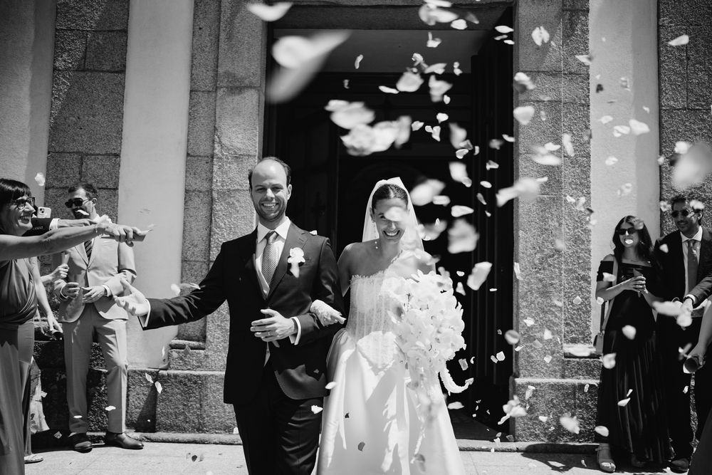Bride and groom exit church amid confetti shower in elegant black and white wedding photo.