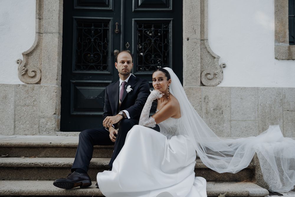 Bride and groom sit on stone steps outside historic building in romantic wedding portrait.