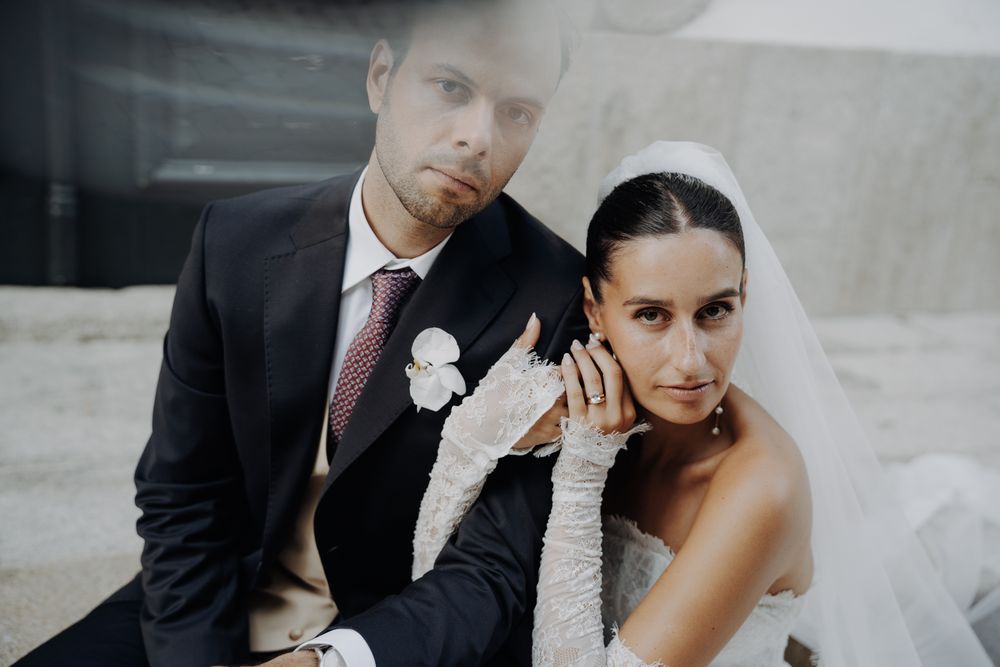 Bride in white gloves and groom in dark suit pose in intimate close-up wedding portrait.