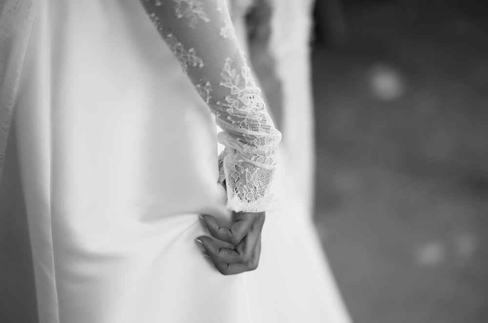 Black and white close-up of a bride in lace wedding dress holding hands with groom.
