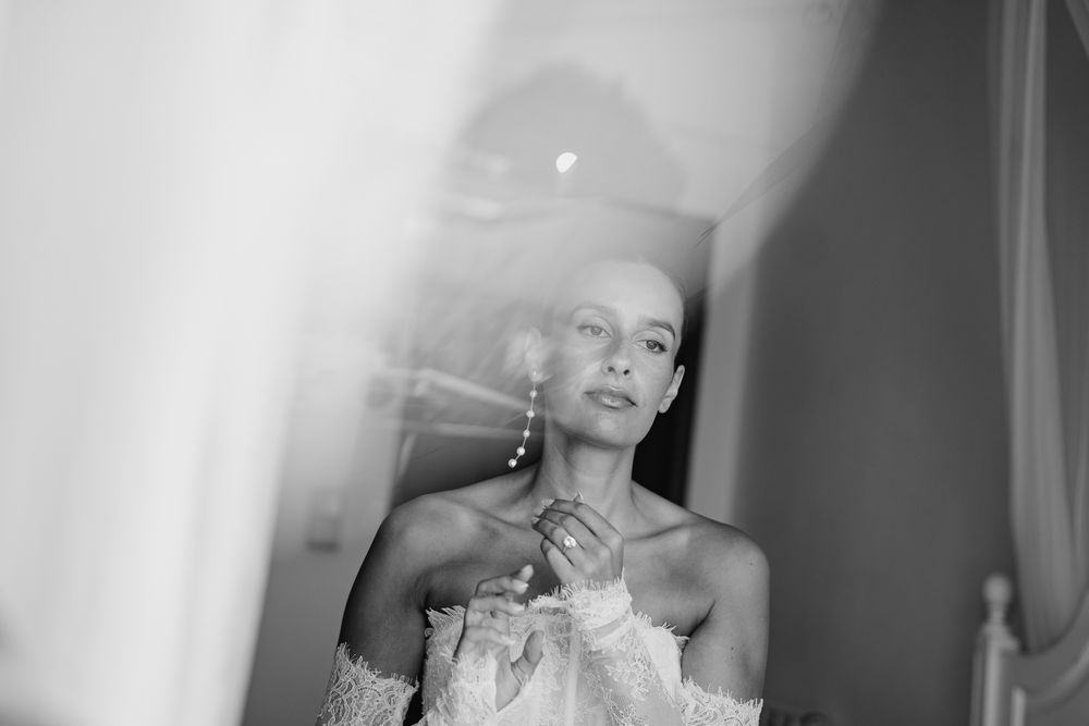 Black and white photo of an elegant woman in off-shoulder dress adjusting pearl earring, soft light.