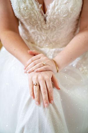 Close-up detail of a sparkly white wedding dress bodice with delicate hands showing an engagement ring.