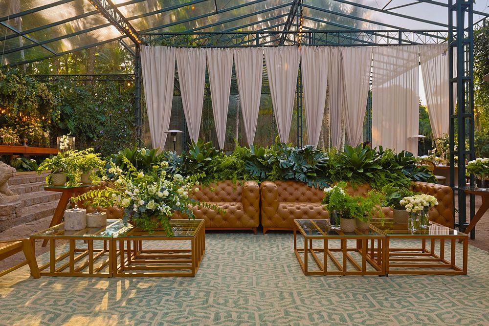 Panoramic shot of an elegant outdoor event space with white drapes, string lights and wooden benches.