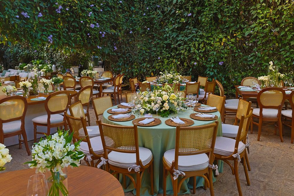 Elegant outdoor dining tables decorated with lush greenery and white floral centerpieces under natural garden lighting.