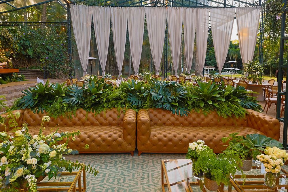 An elegant outdoor event space with cream drapes, brown leather seating, and lush greenery for a garden party atmosphere.