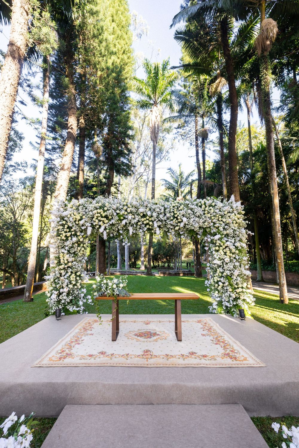 A serene garden path with brick pathways surrounded by tall palm trees and lush flowering white blossoms.