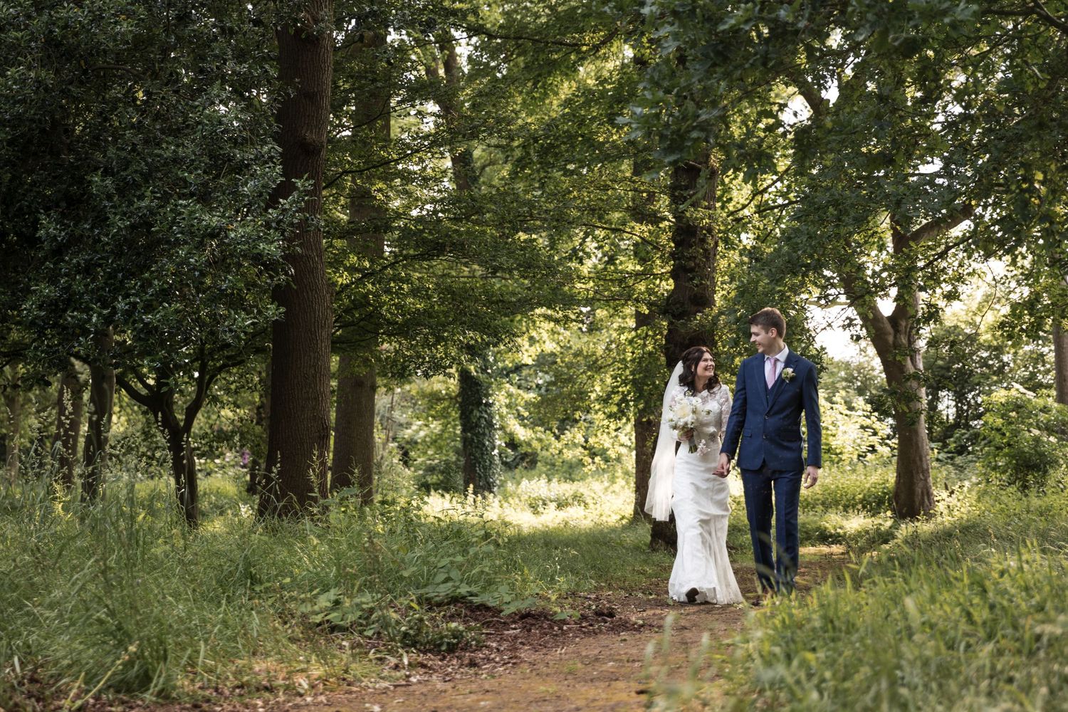 Newlyweds walking hand in hand along the woodland path at Kelham House