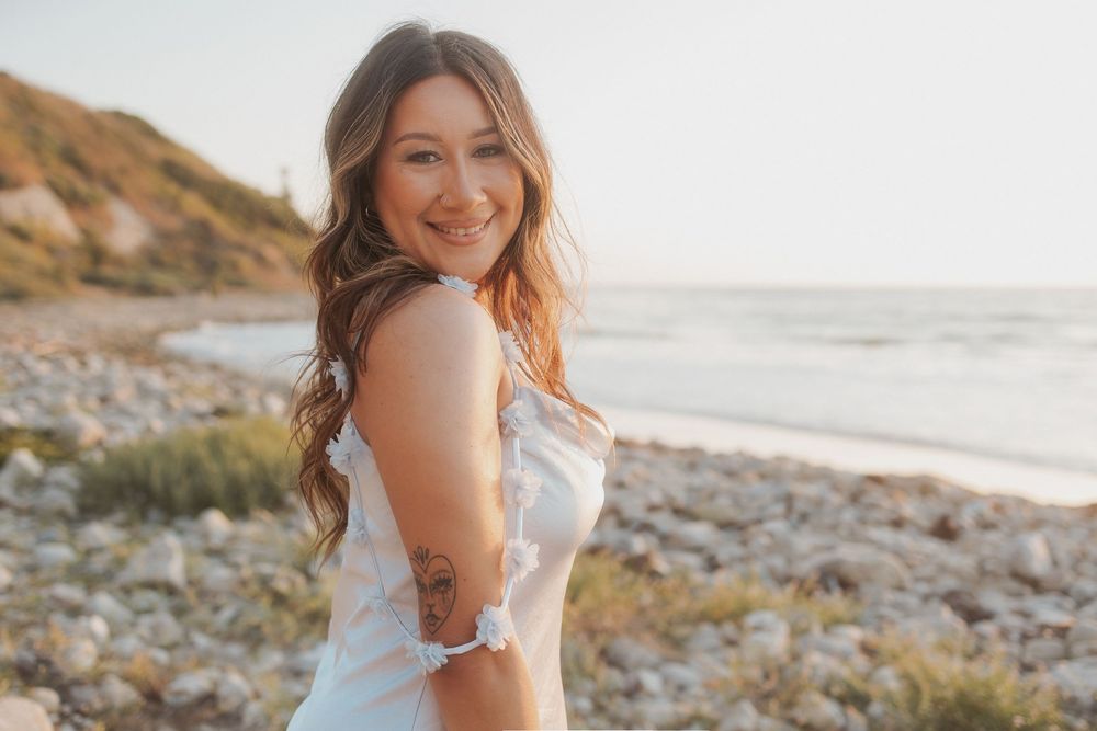 Tropical beach photoshoot featuring a white flowing dress against the rocky coastline at sunset.