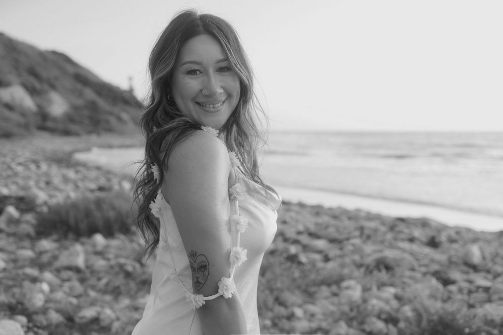A black and white coastal photography session featuring smiling subjects on a rocky beach by the ocean.