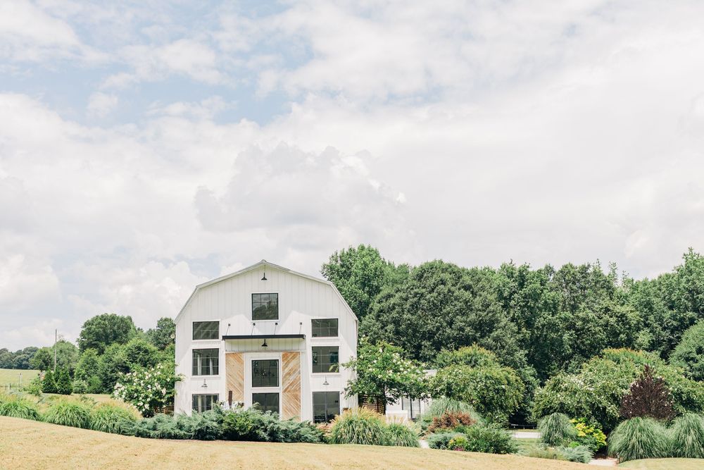 A rural landscape panorama showing Texas ranch buildings and barns with a lush green tree line in the background.