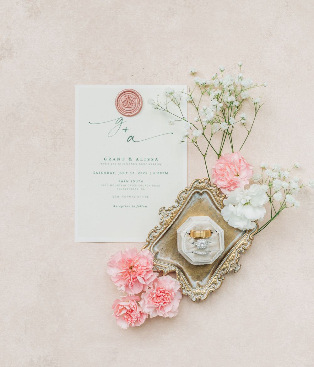 Wedding invitation with pink carnations and jewelry box on antique silver tray against beige background.