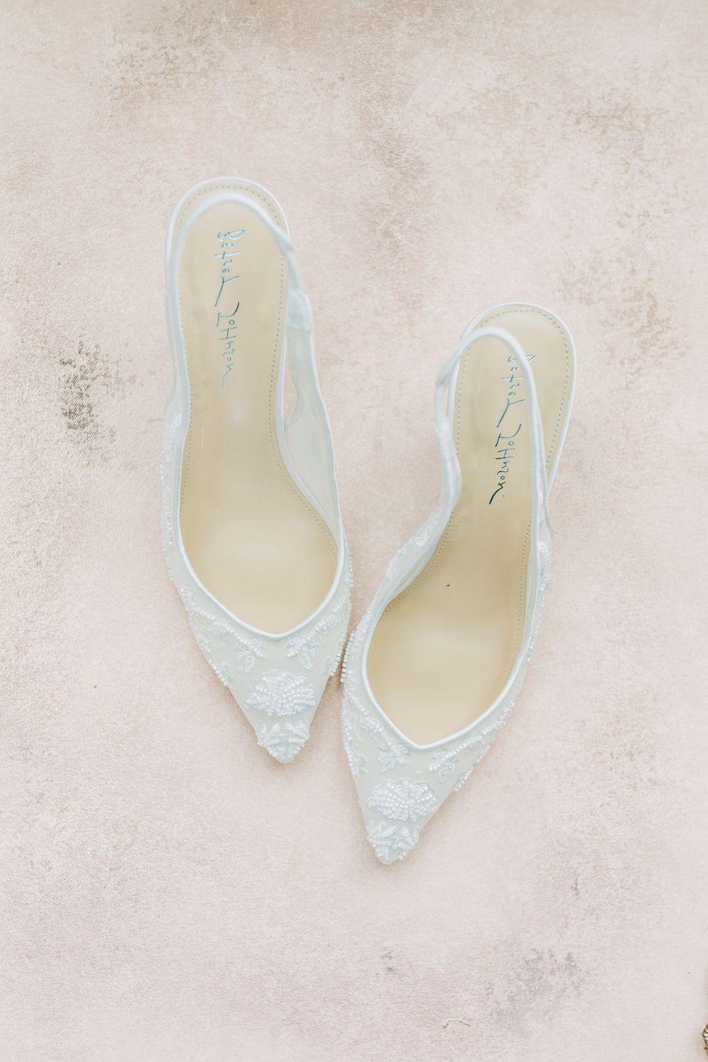 Elegant white lace wedding slingback heels arranged in different angles on a neutral textured background.