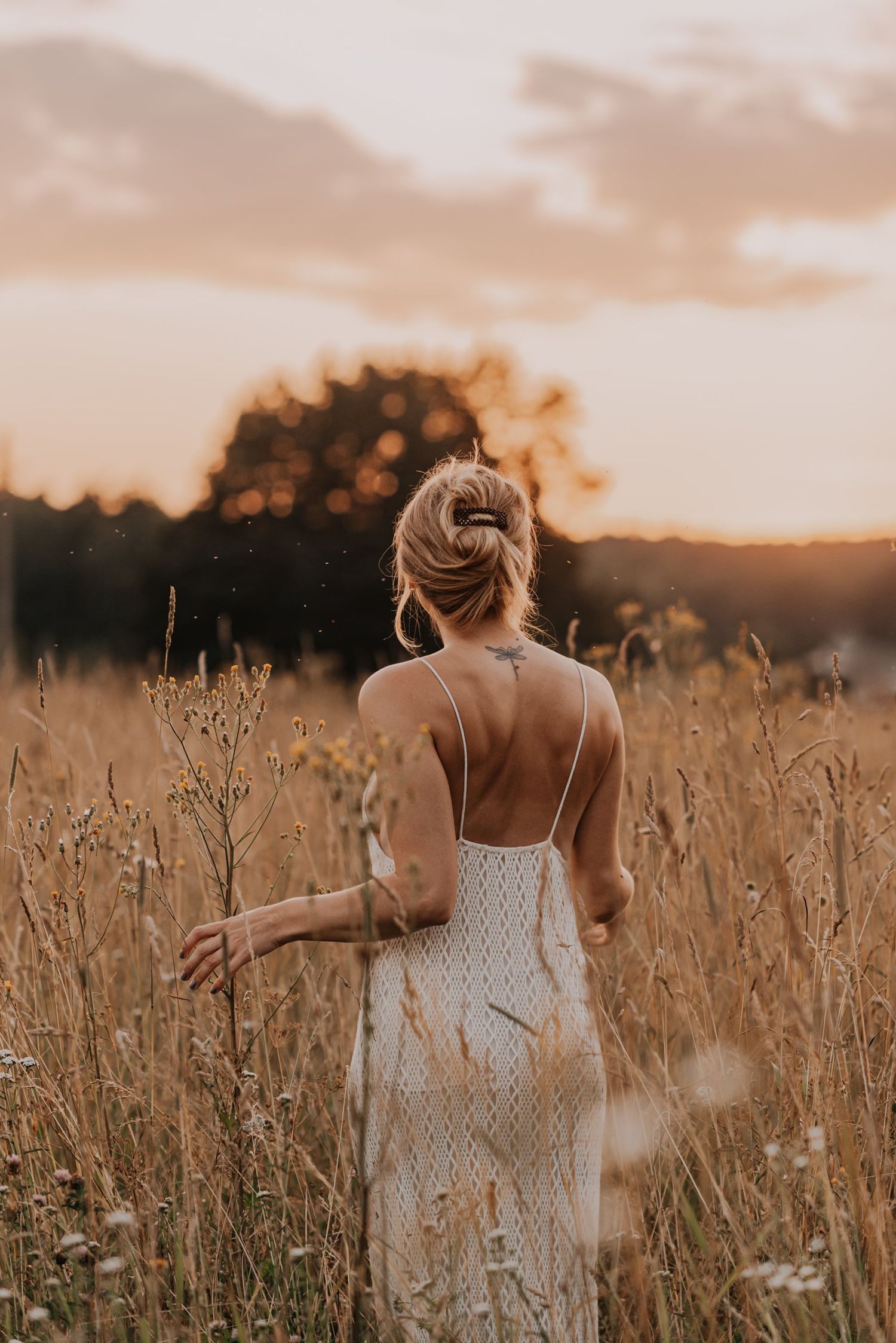 Two people walking through golden field at sunset wearing white dresses.