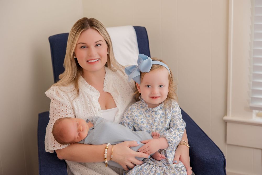 A family portrait in a navy blue armchair showing a parent and children in coordinating light-colored outfits.