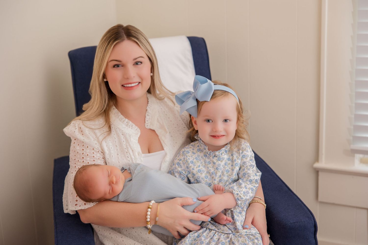 A family portrait in a navy blue armchair showing a parent and children in coordinating light-colored outfits.