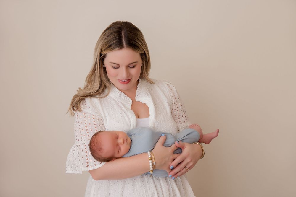 Parent in white lace dress feeding newborn baby while rocking in nursery chair.
