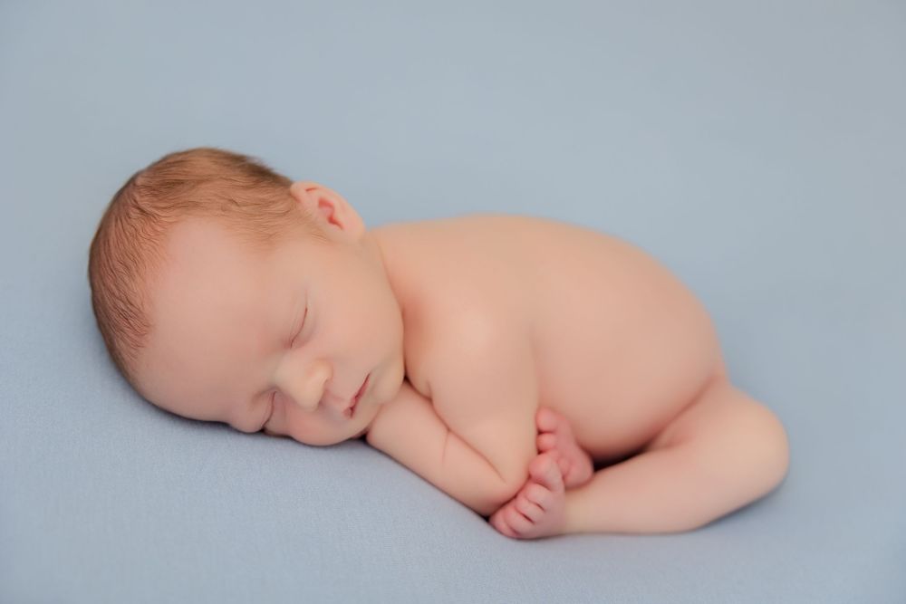 A peaceful sleeping newborn baby curled up on a light blue background during a professional photo session.