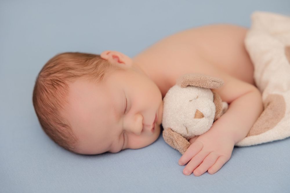 A sleeping newborn baby lies peacefully on soft white textiles in a side-profile photo series.