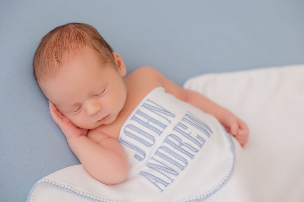Series of peaceful newborn portraits in soft blue and white tones featuring personalized baby apparel.