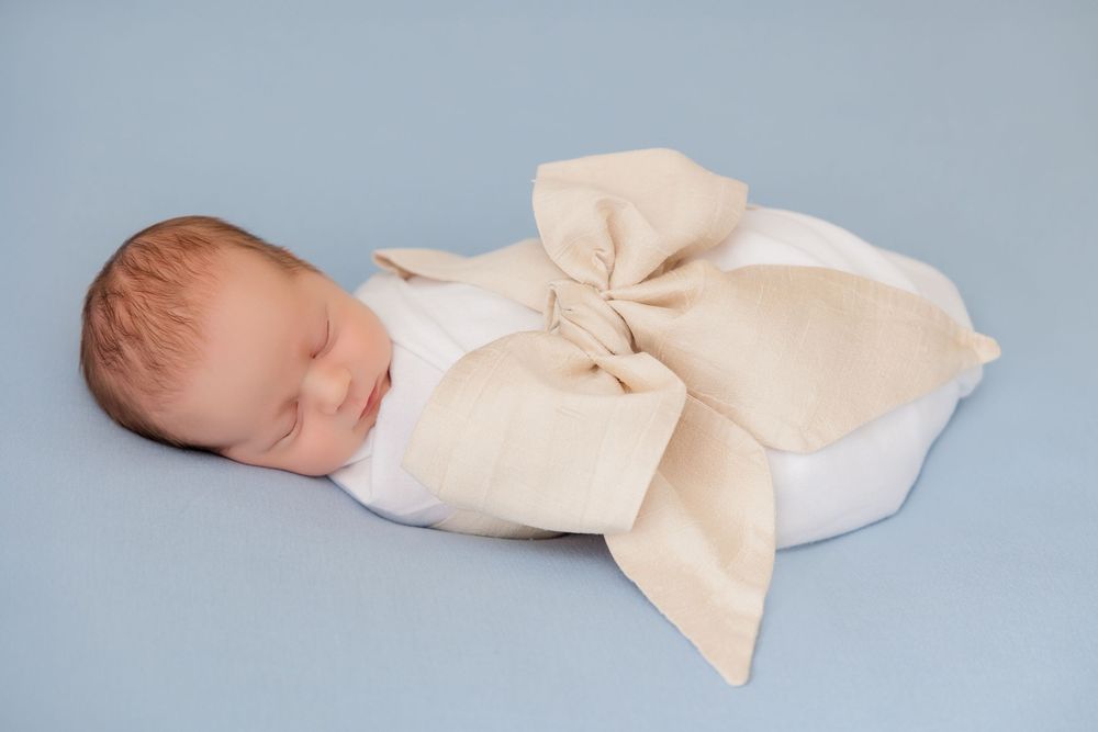 Series of minimalist photos showing a sleeping newborn with large cream bow accessory against blue backdrop.