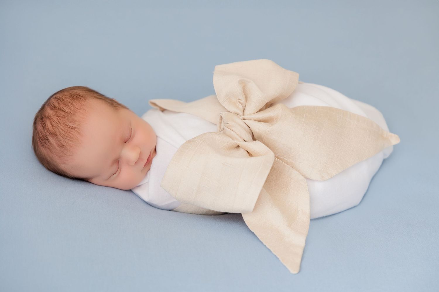 Series of minimalist photos showing a sleeping newborn with large cream bow accessory against blue backdrop.