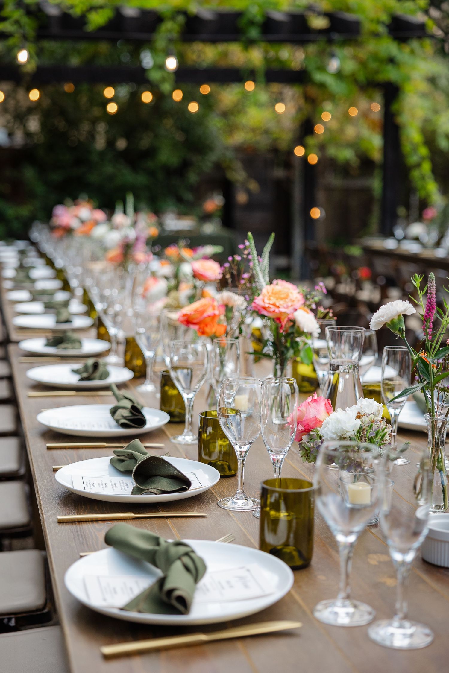 Elegant dining room with rustic wood tables, beige upholstered chairs, and hanging greenery beneath white vaulted ceilings.
