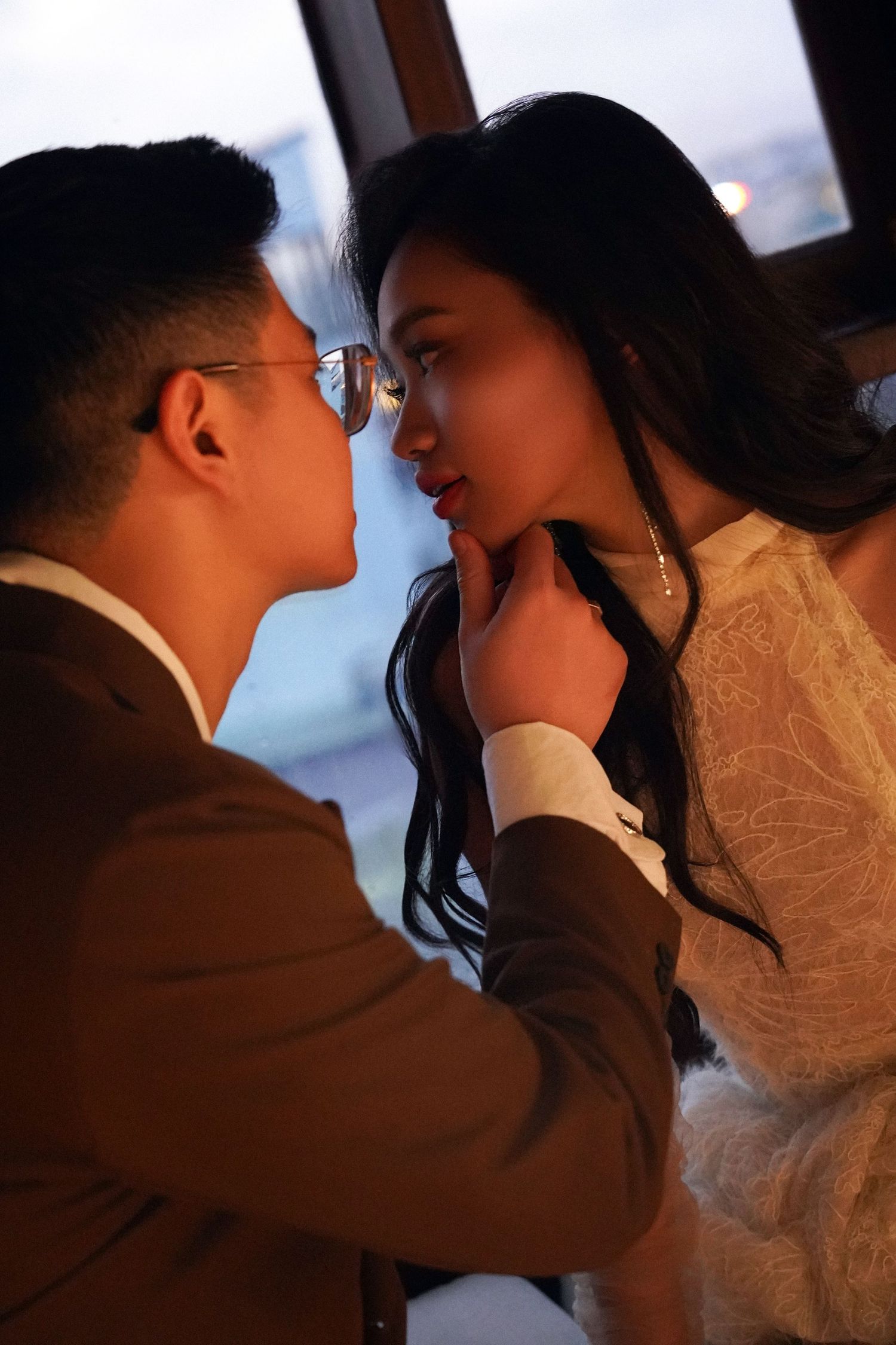 Romantic close-up of Asian couple almost kissing, groom in brown suit gently holding bride's chin.