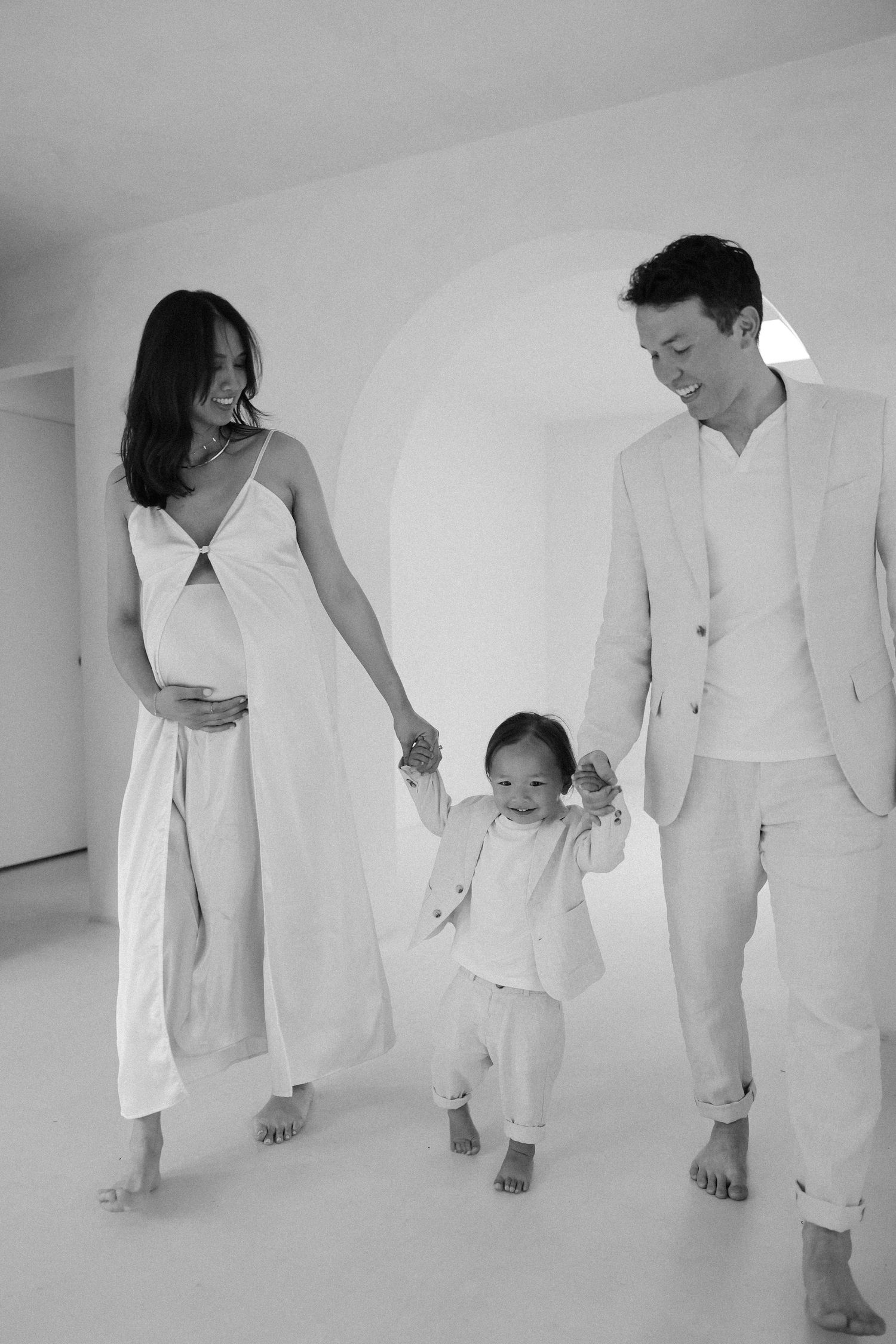 Maternity family photoshoot in LA. A family stands in a minimalist white room with arched doorway