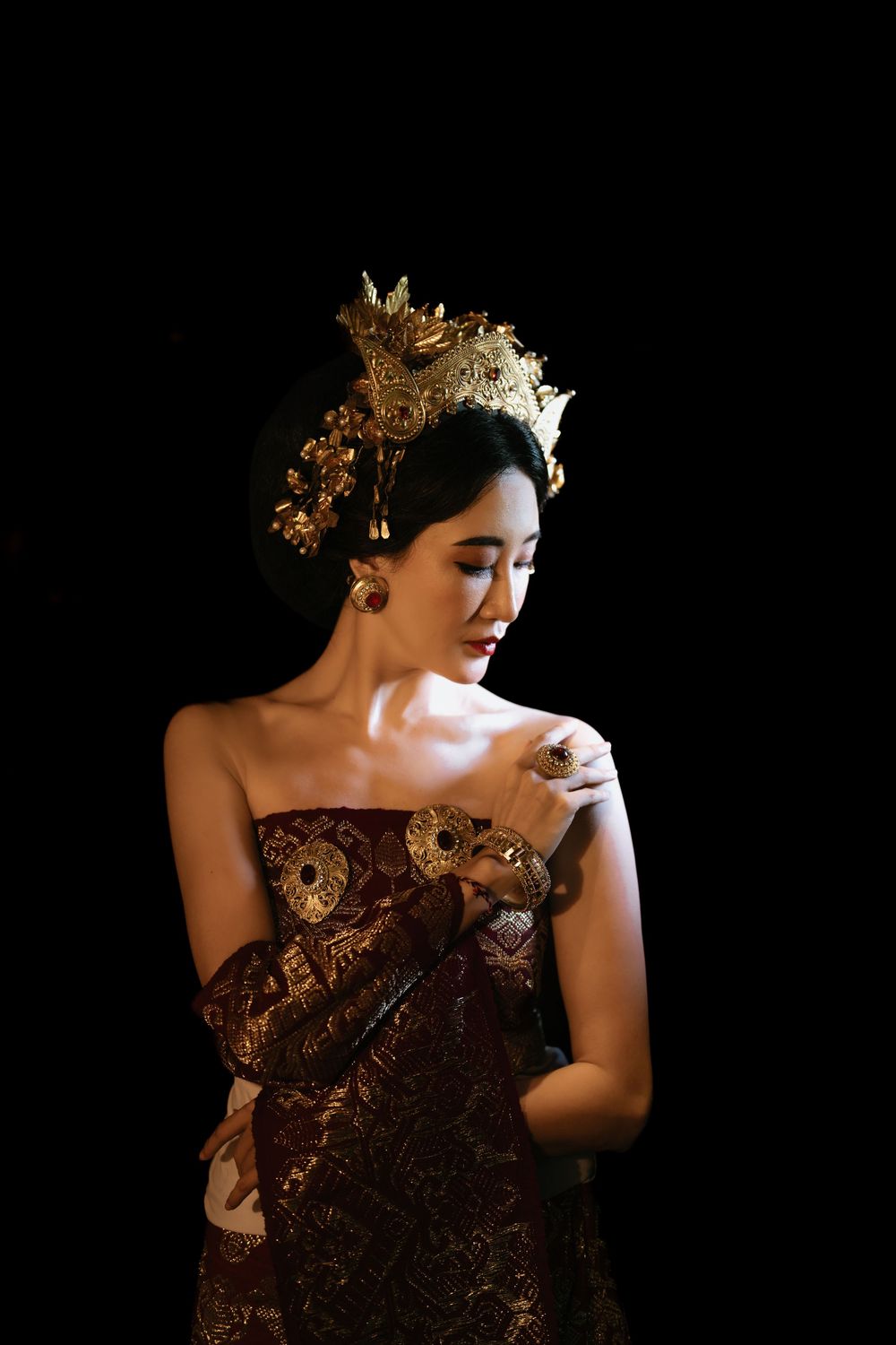 Elegant burgundy dress with gold accessories photographed against dramatic black background.