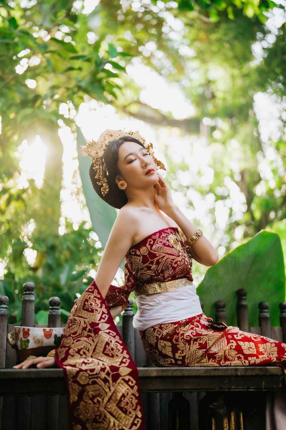 Woman in red batik dress reclining on wooden bench in garden setting.