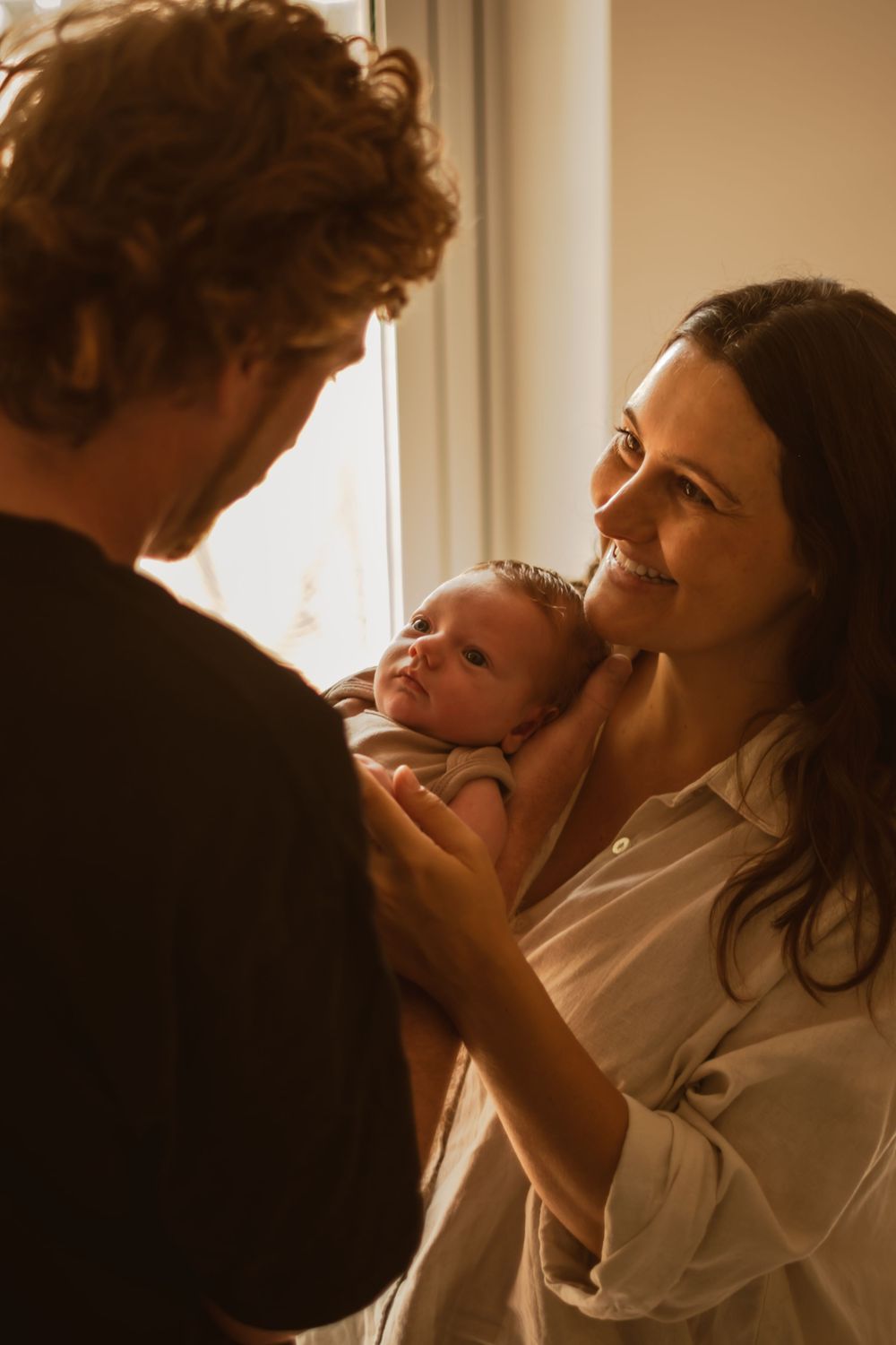 A tender family moment as new parents admire their newborn baby near a sunlit window.