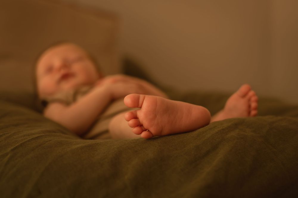 Close-up of tiny baby feet resting on brown fabric in warm lighting.