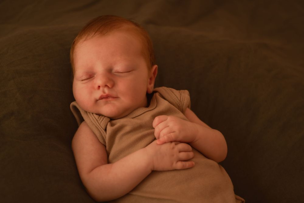 Peaceful sleeping newborn baby wearing beige clothing on dark fabric.