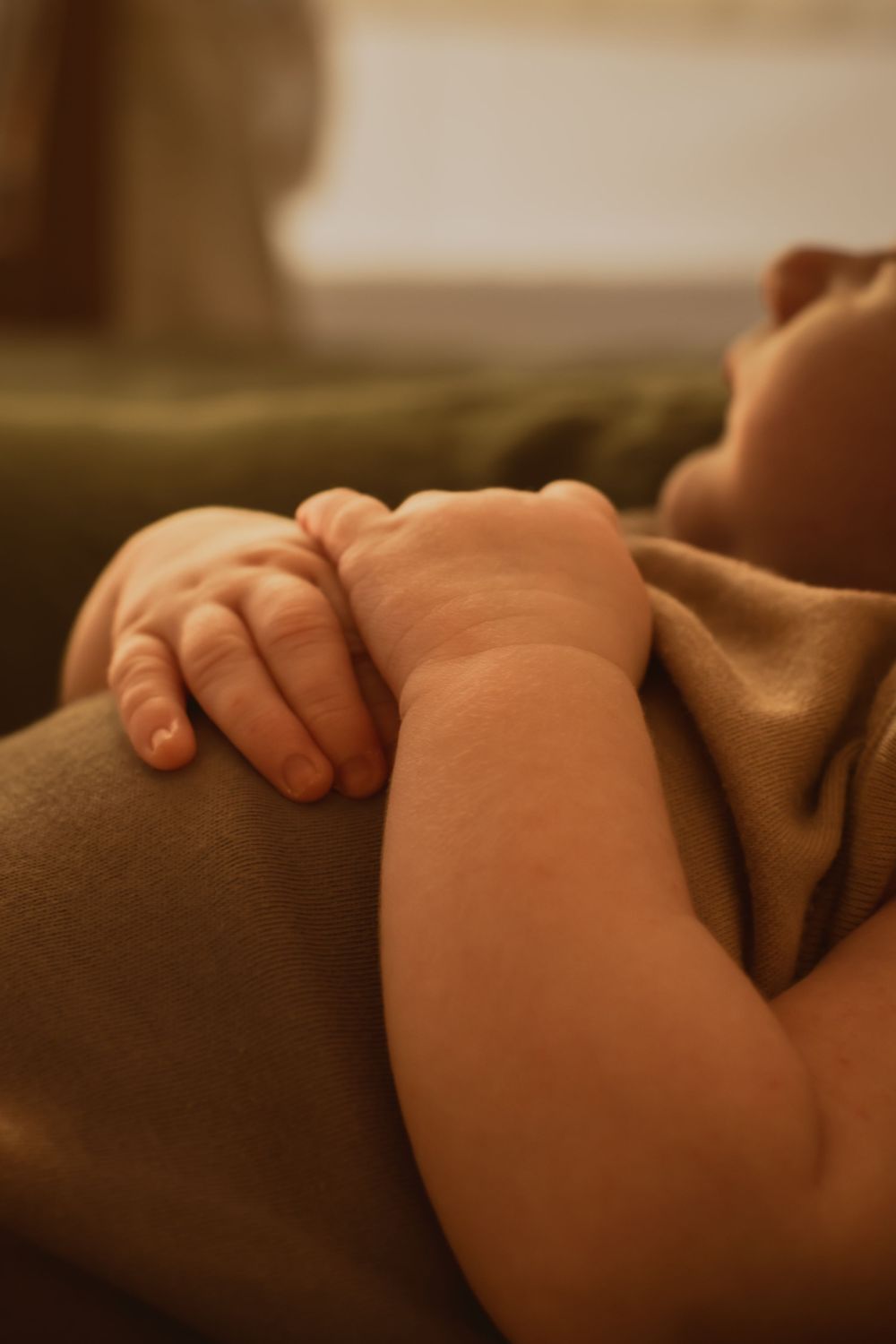 Close-up of a baby's hand resting gently on brown fabric.