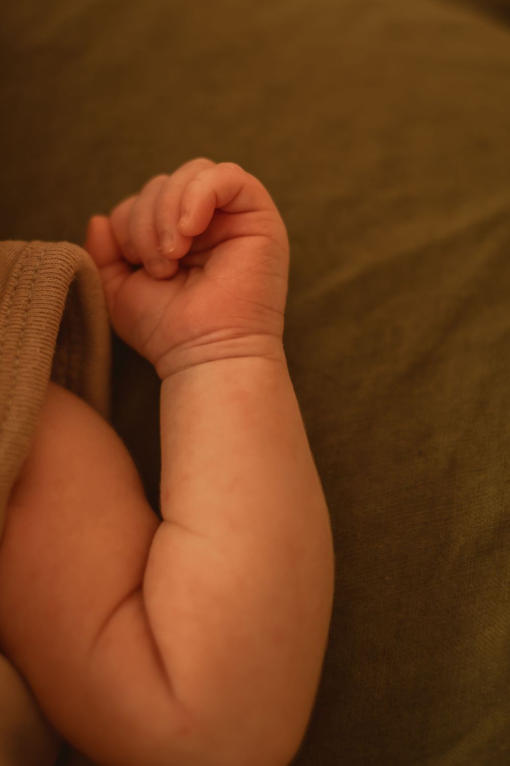 Close-up of a baby's arm and tiny fist against brown fabric.