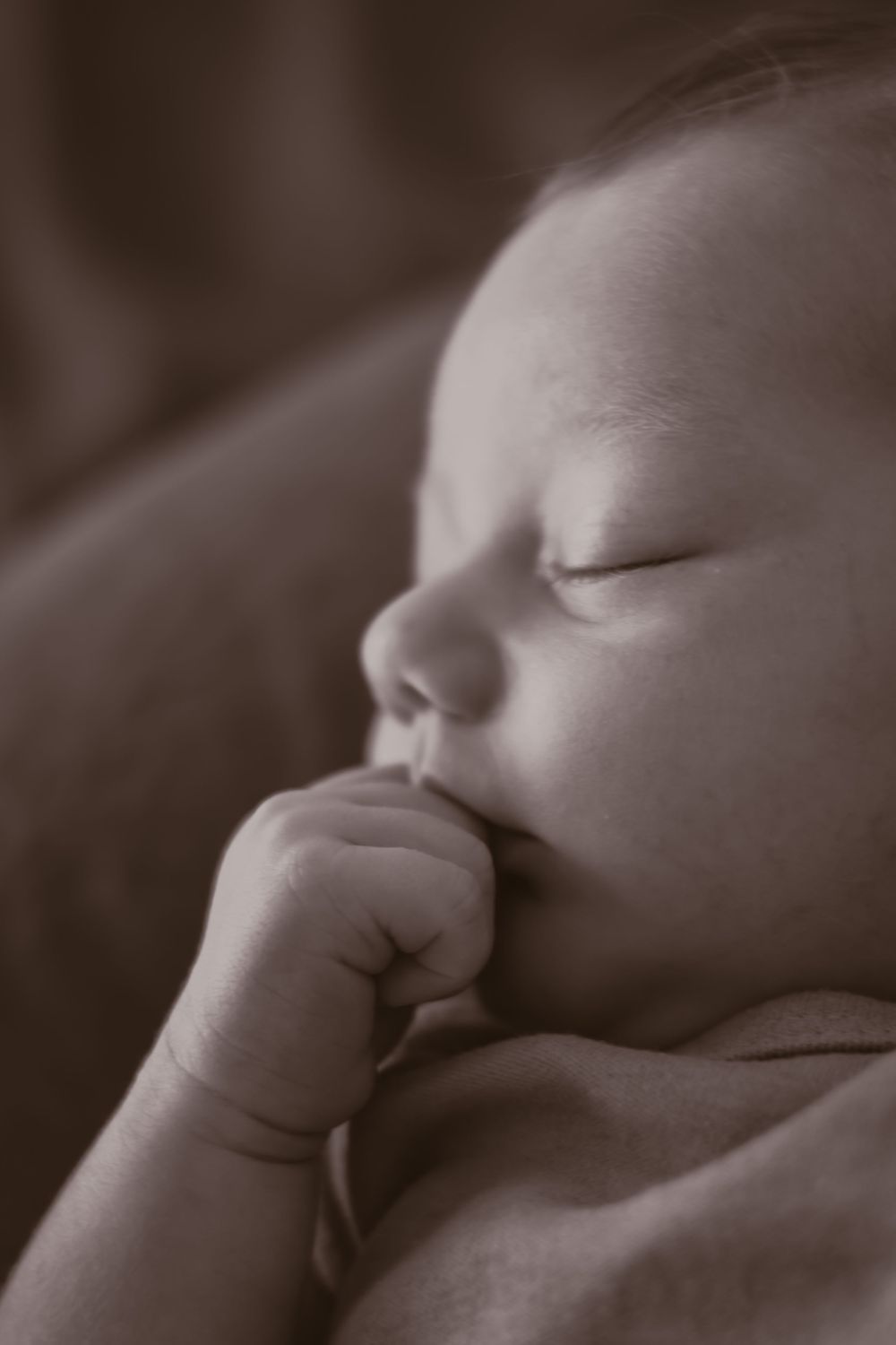 Serene close-up of a sleeping baby with thumb near mouth.